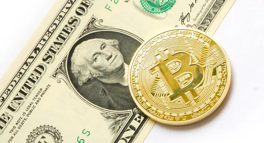 A physical bitcoin token resting on a US one dollar bill, illustrating the exchange of dollars for cryptocurrency