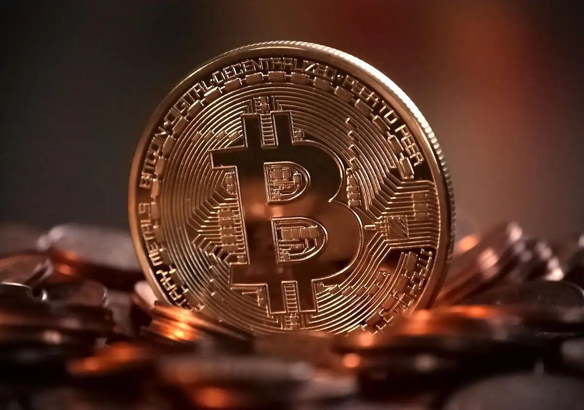 A gold-coloured bitcoin token photographed close up under warm light, resting on other coins