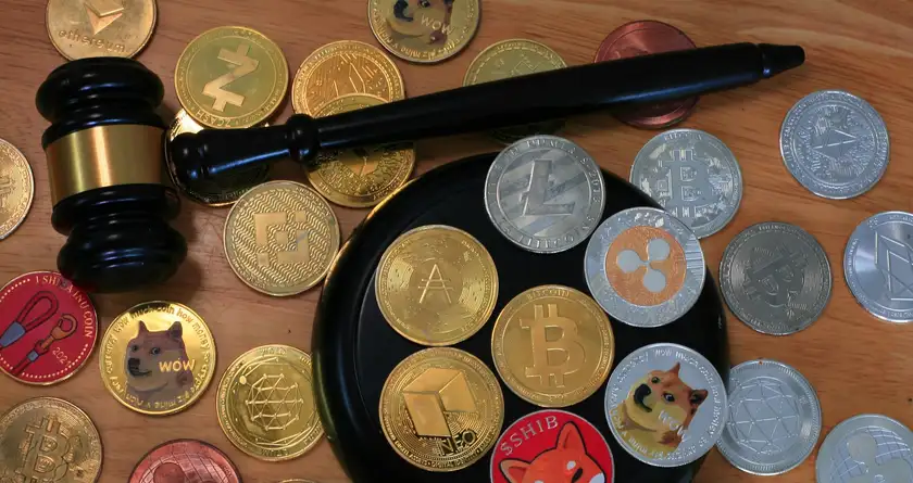 A judge's gavel resting among an assortment of physical cryptocurrency tokens